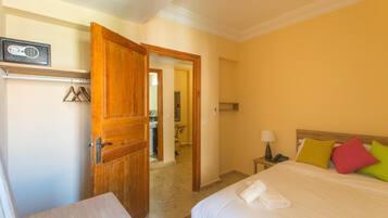 Une chambre d’hôtel avec un lit, une porte en bois, une table de chevet et une salle de bain visible à travers une porte ouverte.