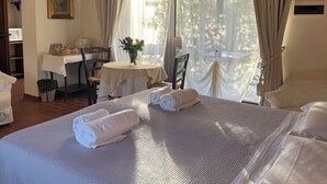 Een slaapkamer met een groot bed, een klein tafeltje met een bloemenvaas en een stoel.
