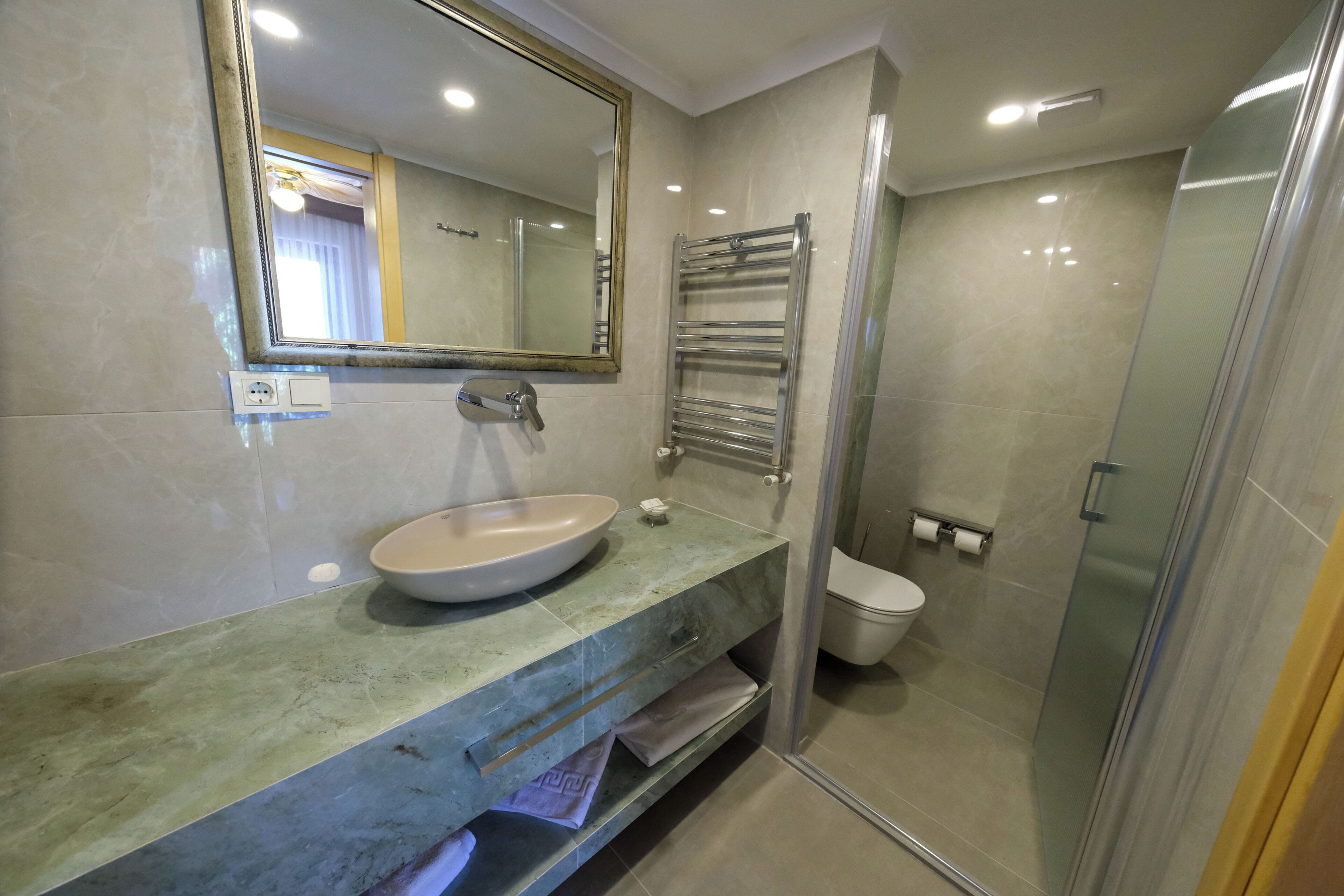 Un baño con lavabo, espejo, toallero, inodoro y cabina de ducha de vidrio.