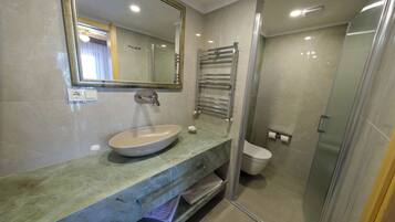Un baño con lavabo, espejo, toallero, inodoro y cabina de ducha de vidrio.