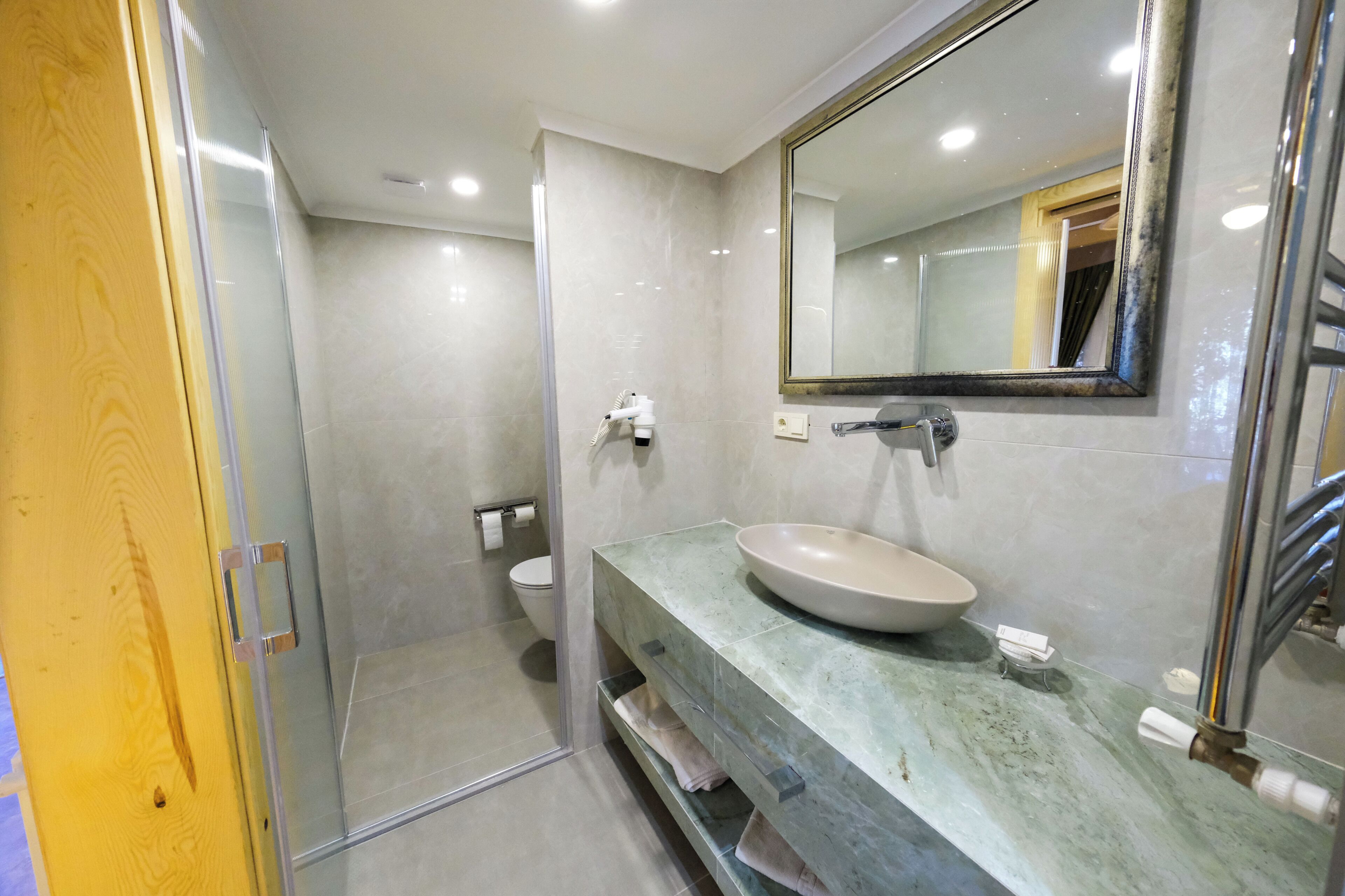 A bathroom with a glass shower enclosure, a sink with a marble countertop, and a large mirror.