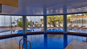 Piscina interior com vista direta para o mar, cadeiras de descanso e área ao redor da piscina.