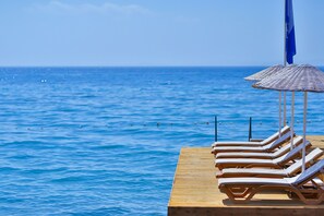 Una terraza de madera con tumbonas y una sombrilla azul, con vista a un mar tranquilo.
