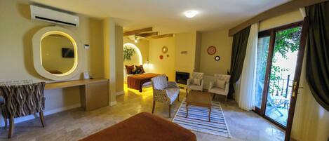 Habitación de hotel con cama, zona de estar con sofá y sillones, mesa de comedor y un gran ventanal con cortinas.