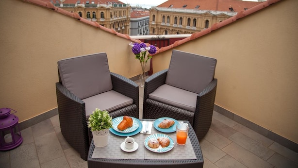 Un balcón con mobiliario de mimbre, una mesa con platos de comida, una bebida y una planta en maceta.