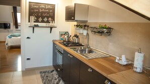 Cocina compacta con estufa a gas, lavamanos y encimera de madera. Hay plantas colgantes y una pizarra con escritura en la pared.