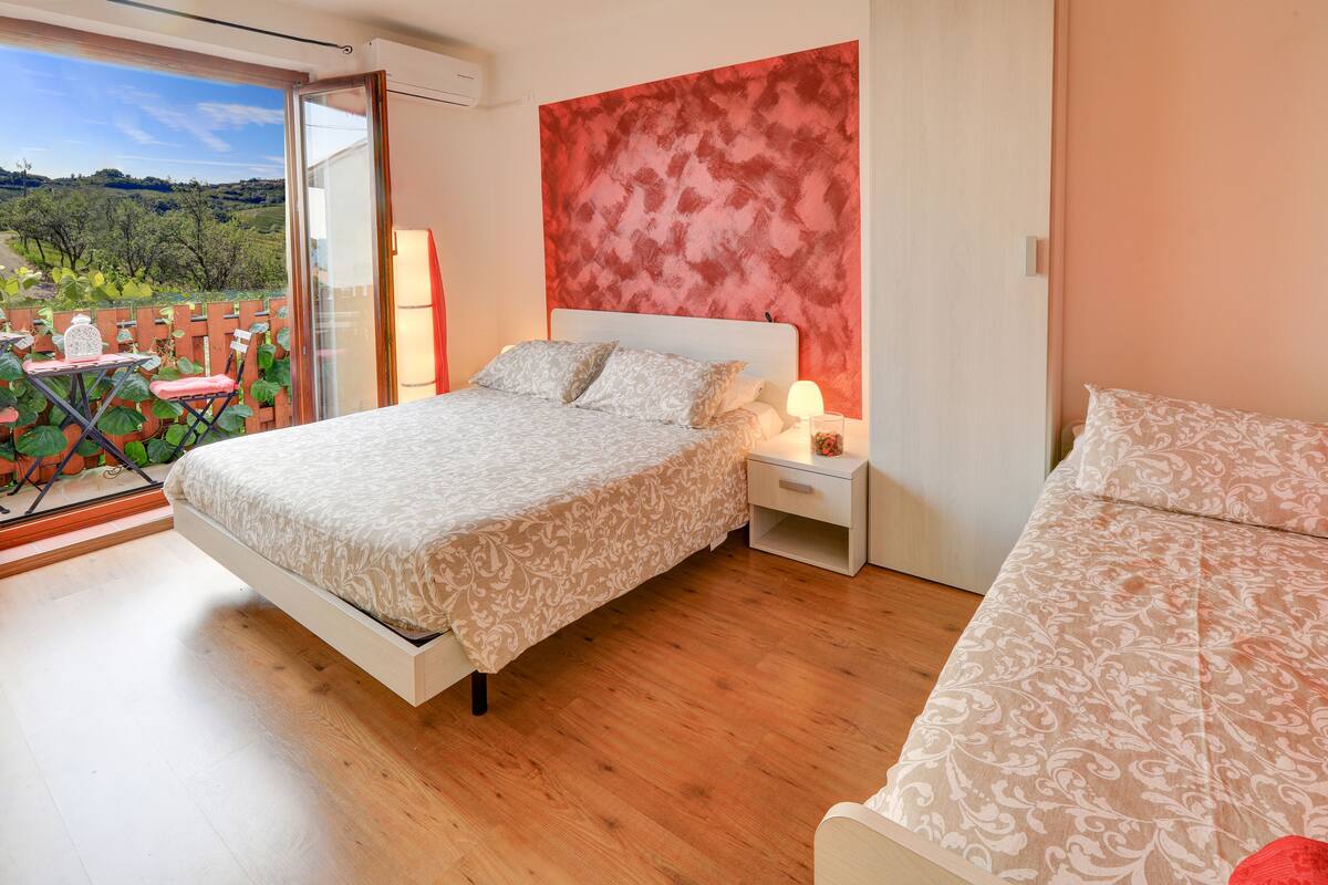 A bedroom with a bed, a nightstand, a window, and a view of the outdoors.