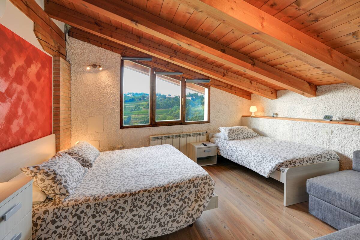 A bedroom with two beds, a wooden ceiling, and a view of the countryside.