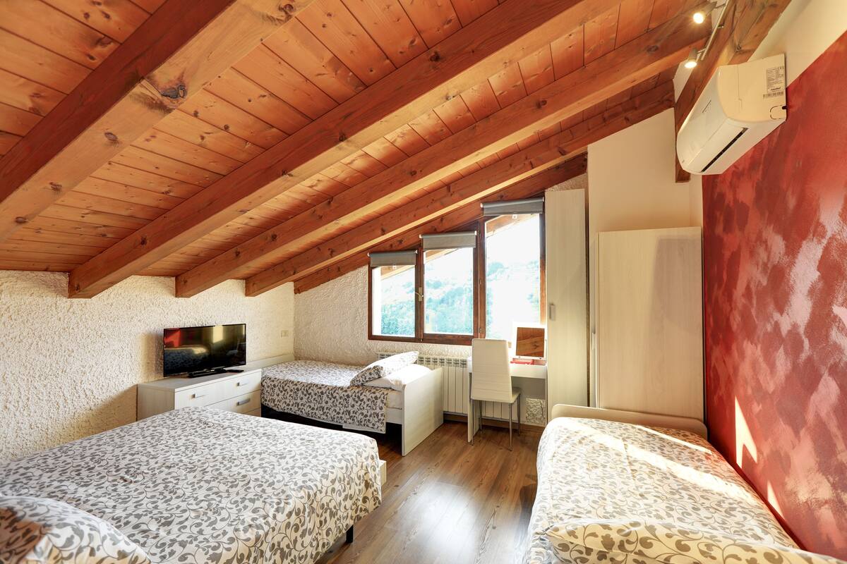 A bedroom with two beds, a desk, a chair, a television, and a window.