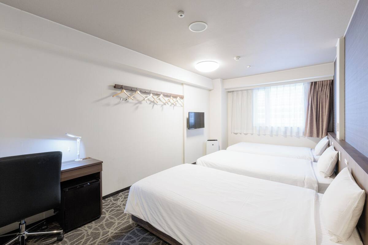 A hotel room with two beds, a desk with a lamp, a TV, and a coat rack.