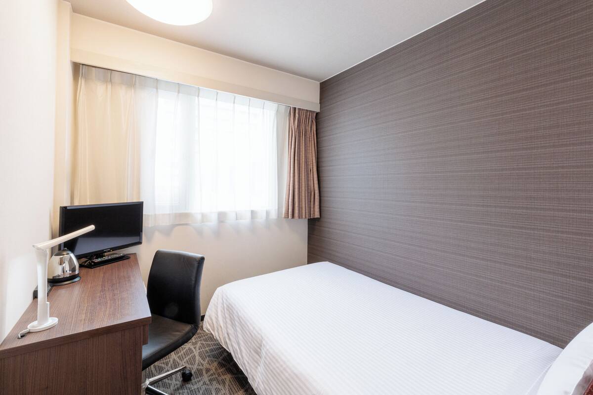 A hotel room with a bed, a desk with a computer, a chair, and a television.