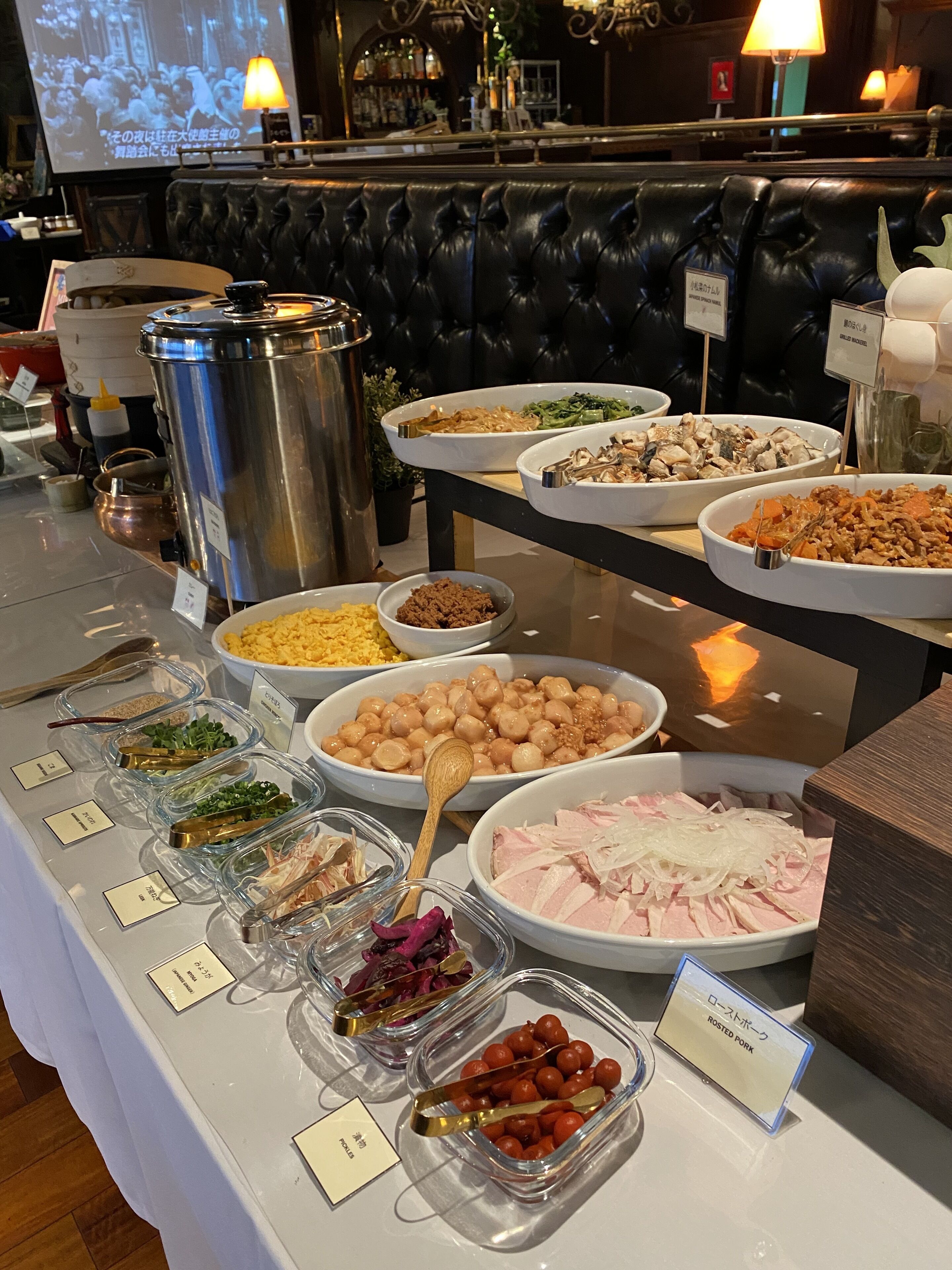Un bufé con diversos platos, entre ellos carne de cerdo asada, vegetales y otros alimentos ya preparados.