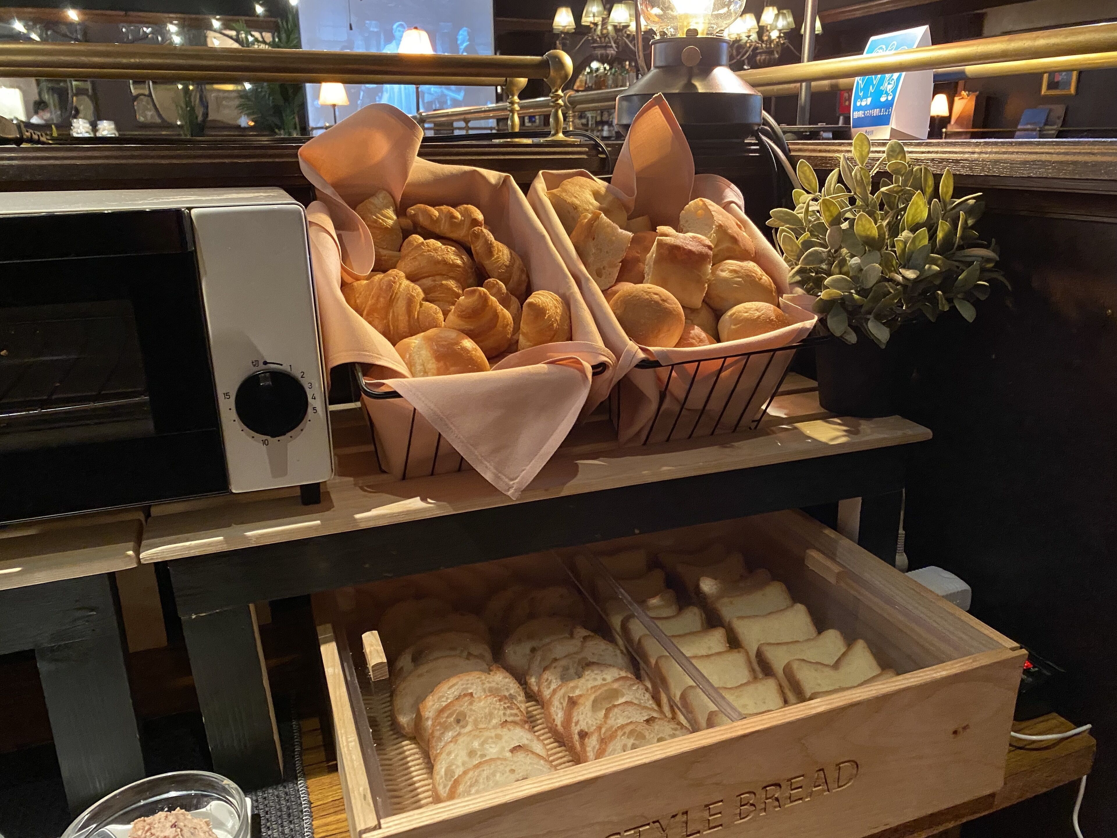 En bageridisplay med brød og kager, en kaffemaskine og en potteplante.
