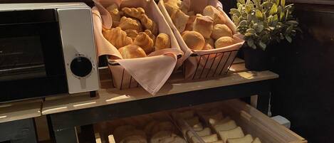 A bakery display with bread and pastries, a coffee machine, and a potted plant.