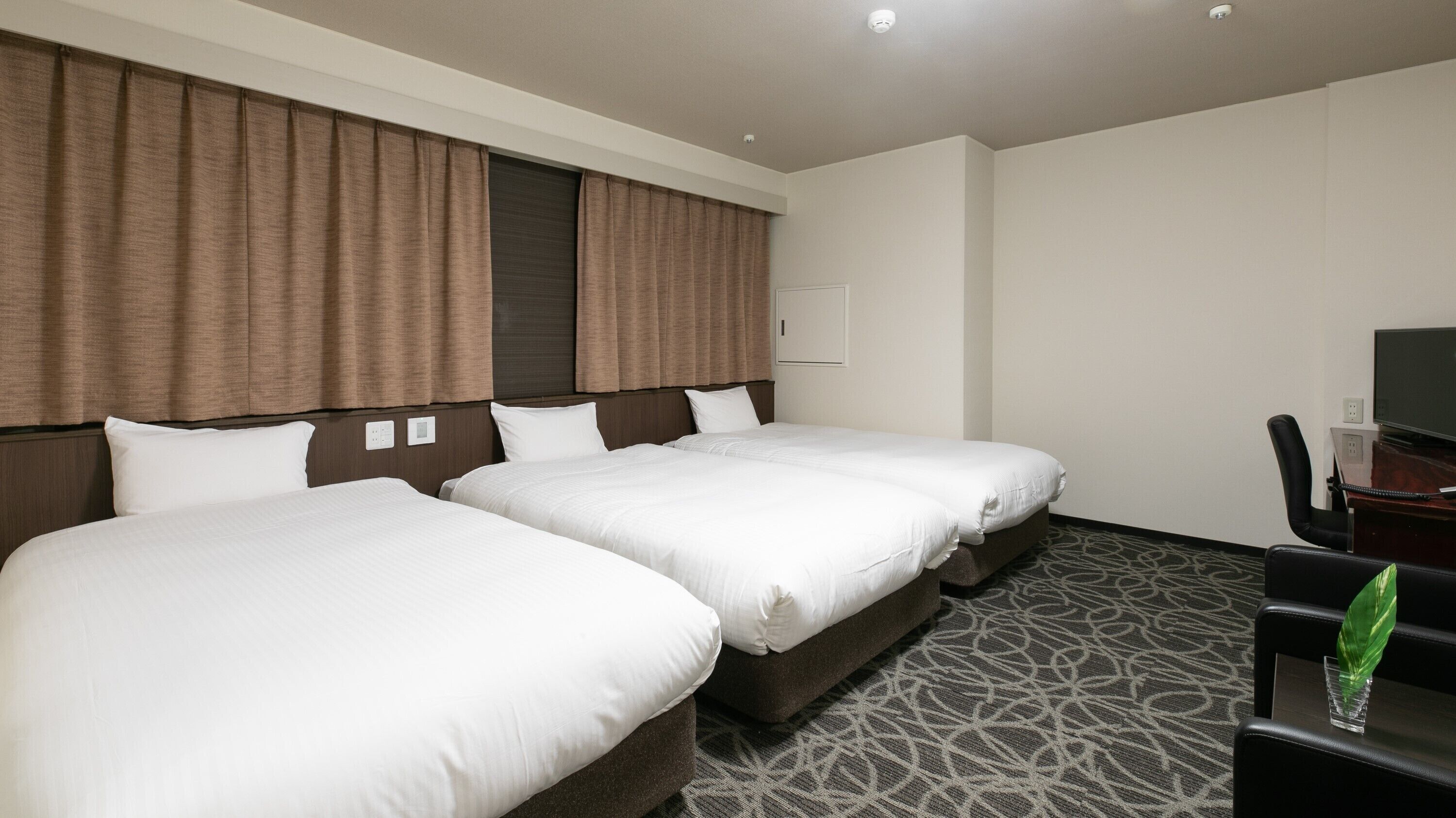A hotel room with two beds, a desk, a chair, and a television.