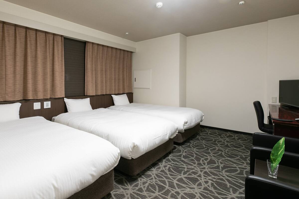 A hotel room with two beds, a desk, a chair, and a television.