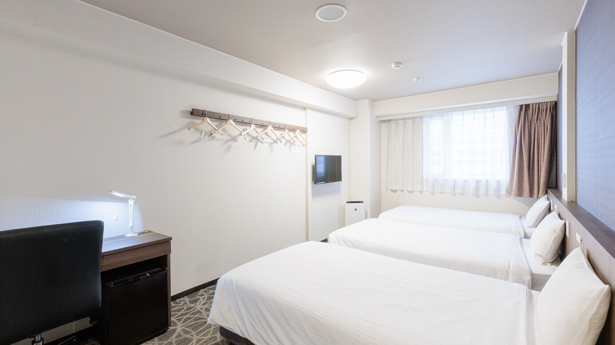Een hotelkamer met twee bedden, een bureau met lamp, een televisie en een kapstok.