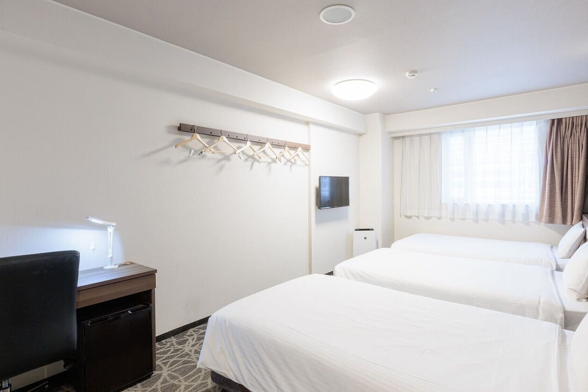 Une chambre d’hôtel avec deux lits, un bureau avec une lampe, une télévision et un porte-manteau.