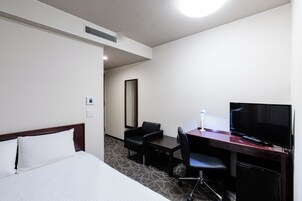 A hotel room with a bed, a desk with a TV, a chair, and a small table.