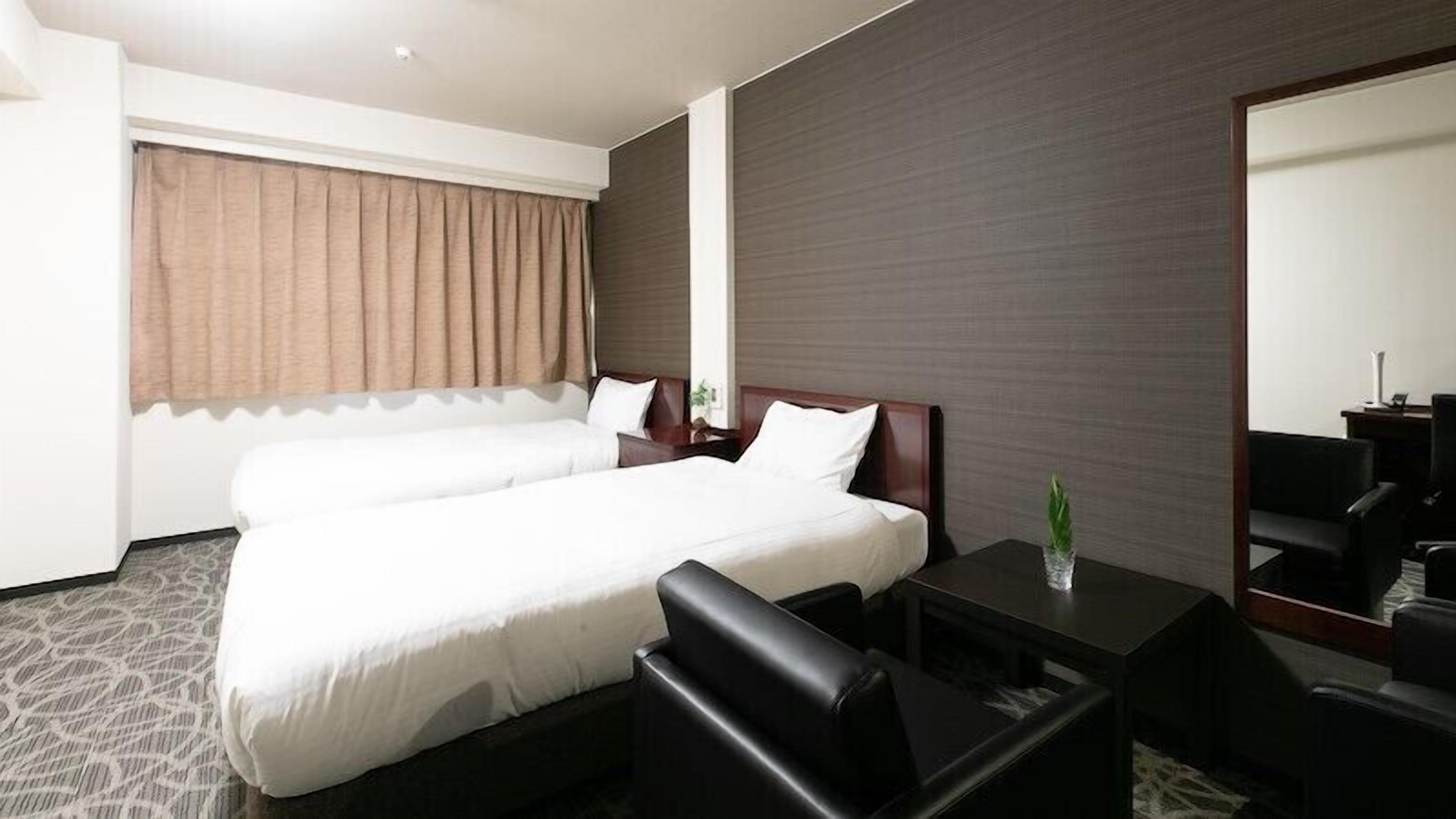 A hotel room with a double bed, a desk, a chair, a mirror, and a window with curtains.