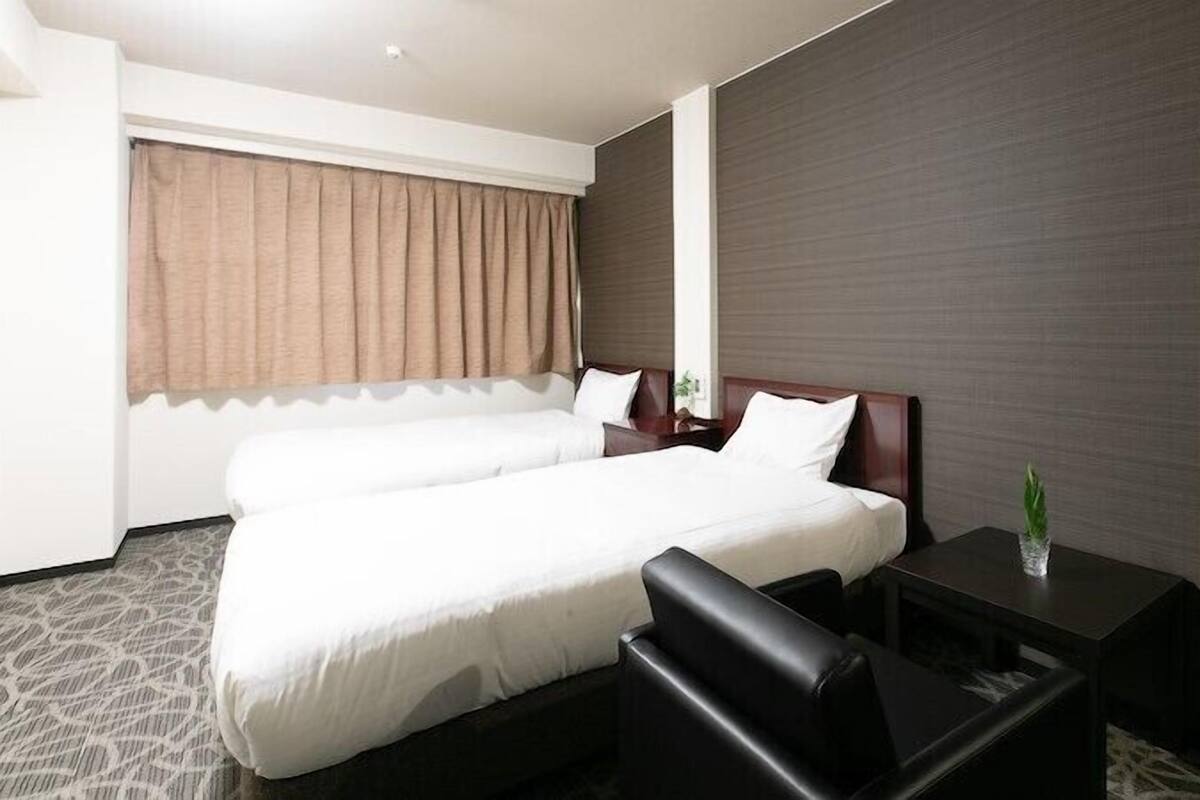 A hotel room with a double bed, a desk, a chair, a mirror, and a window with curtains.