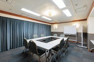 Un salón de conferencias con una mesa rectangular, seis sillas, una pizarra y una pantalla de proyección.