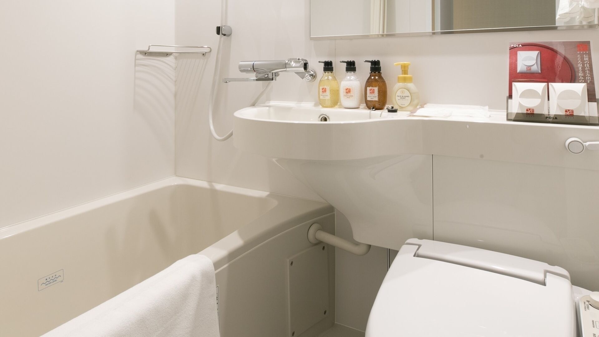 A bathroom with a bathtub, a sink with toiletries, a mirror, and a toilet.