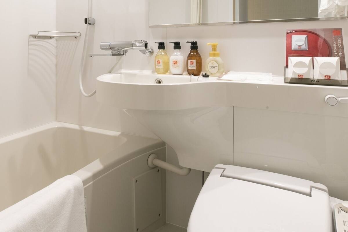 A bathroom with a bathtub, a sink with toiletries, a mirror, and a toilet.