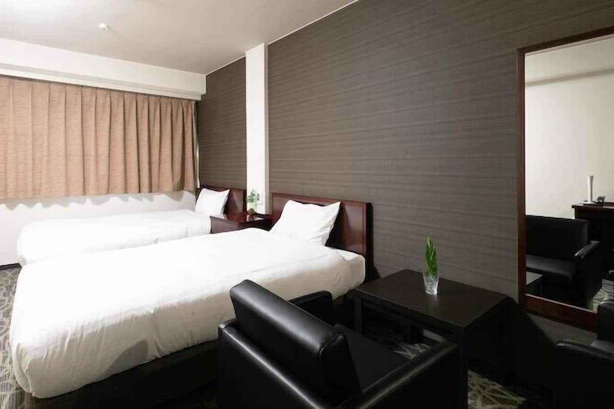 Une chambre d’hôtel avec un lit double, un bureau, une chaise, un miroir et une fenêtre avec des rideaux.