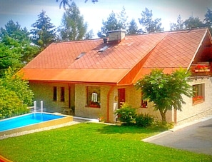 Une maison avec un toit recouvert de tuiles rouges, une piscine et une pelouse bien entretenue.