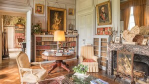 A library with bookshelves, a fireplace, and a portrait. - Château de Boucéel (Saint-James)
