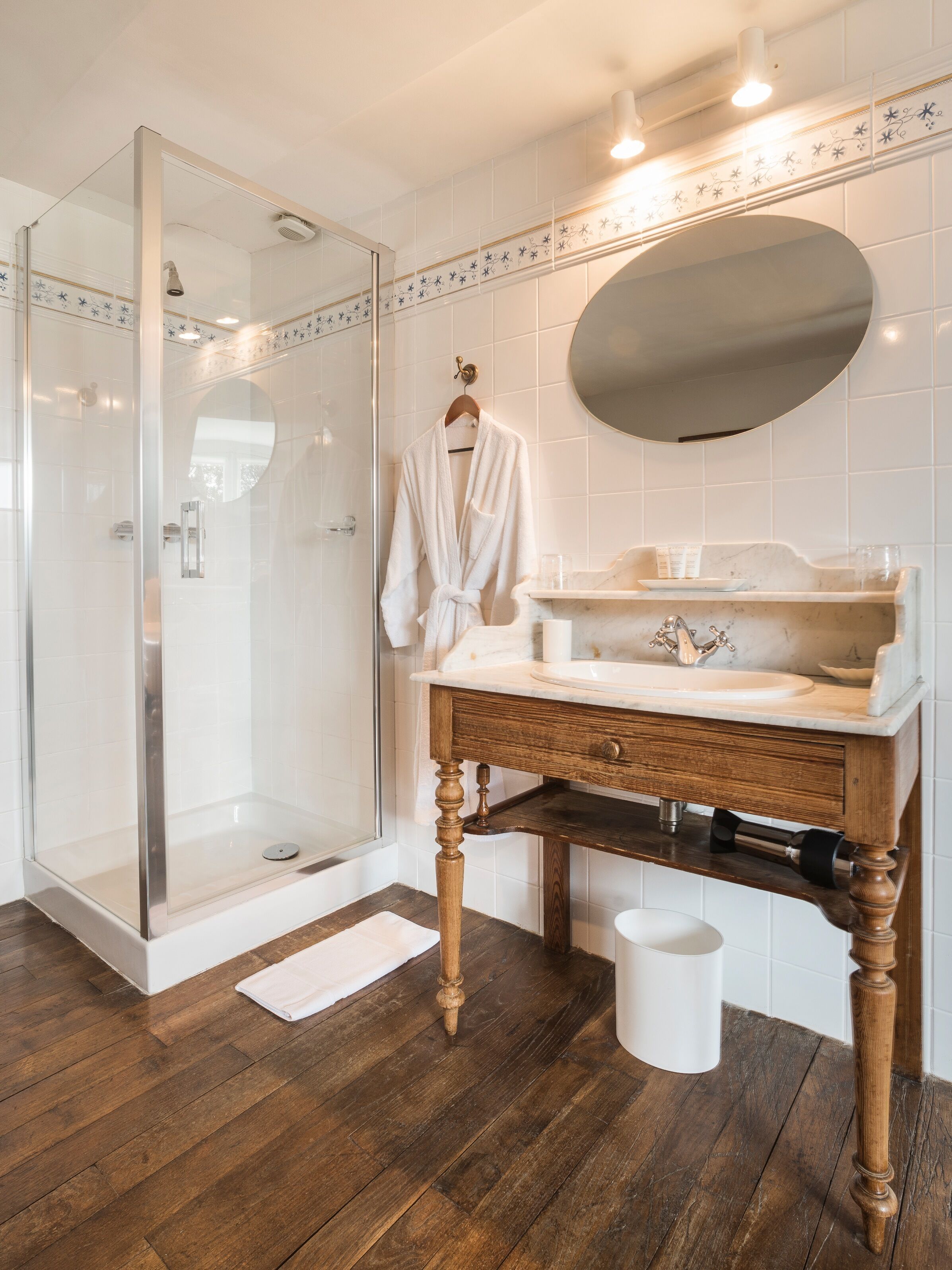 Een moderne badkamer met een douchecabine van glas, een houten wastafelmeubel met een marmeren blad en een grote spiegel.