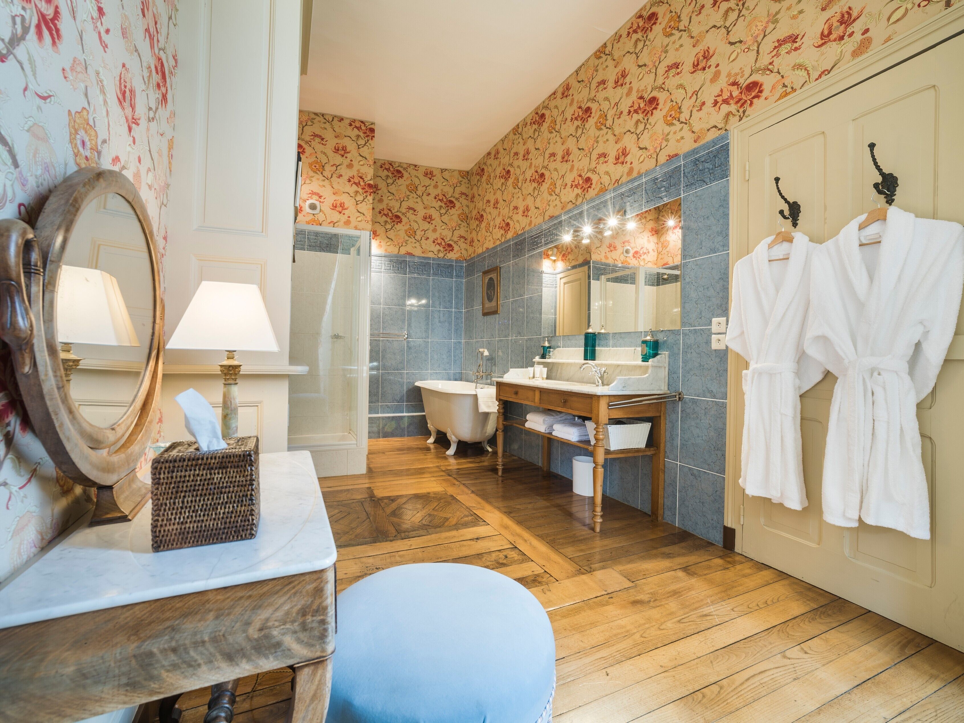 A bathroom with a wooden vanity, a freestanding bathtub, a large mirror, and a towel rack with robes.