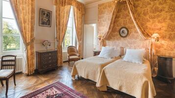 Une chambre à coucher de style traditionnel, avec deux lits, un plancher en bois, un radiateur, une chaise, une commode et une fenêtre avec des rideaux.