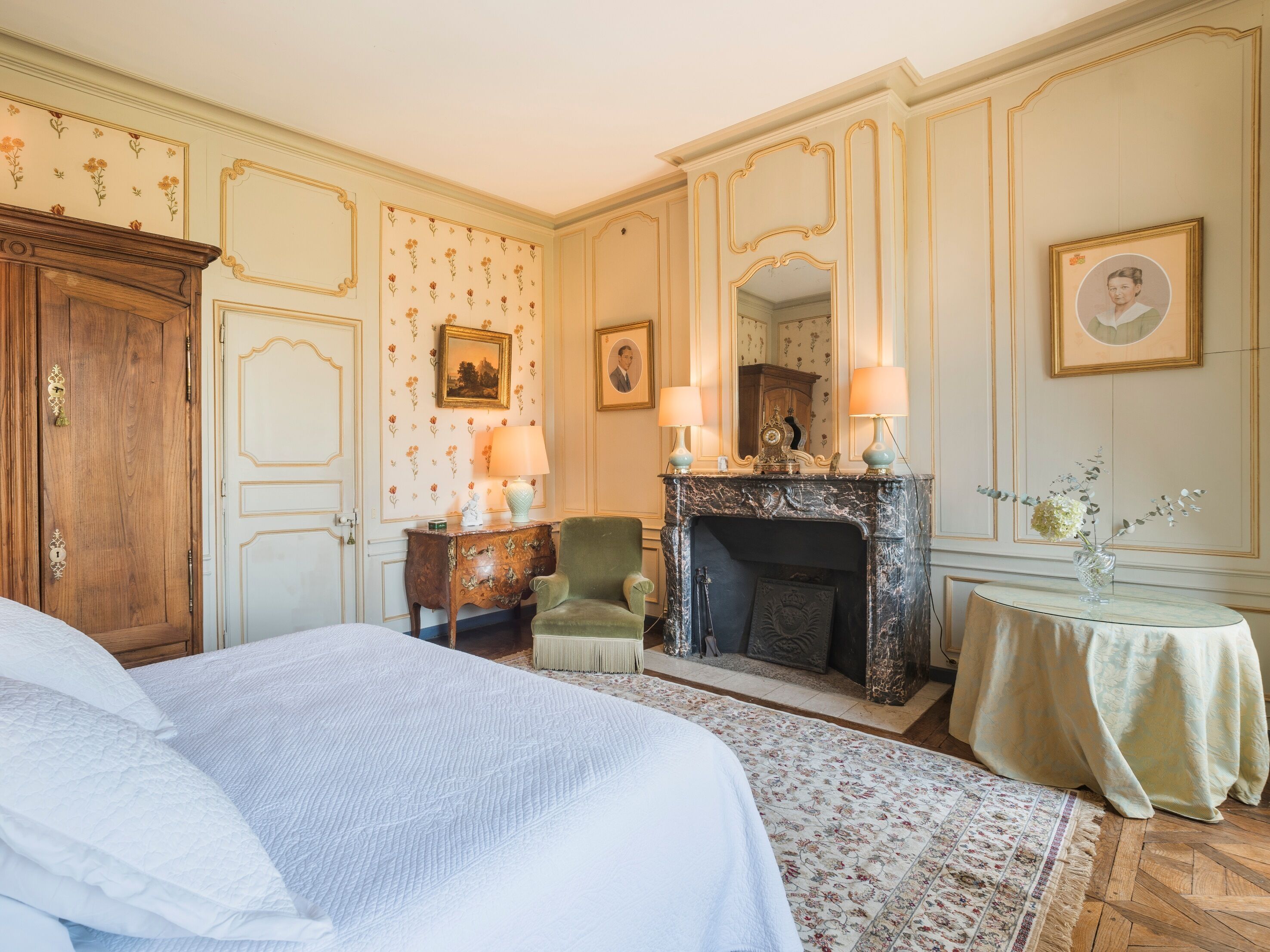 A classic room with a large bed, a fireplace, and a small table with a vase.