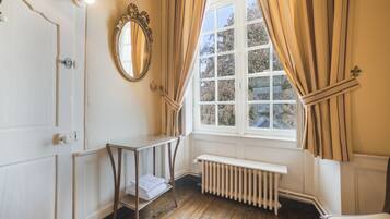 Ein Zimmer mit Holzboden, einem weißen Heizkörper, einer Bank, einem Spiegel und einem Fenster mit Vorhängen.