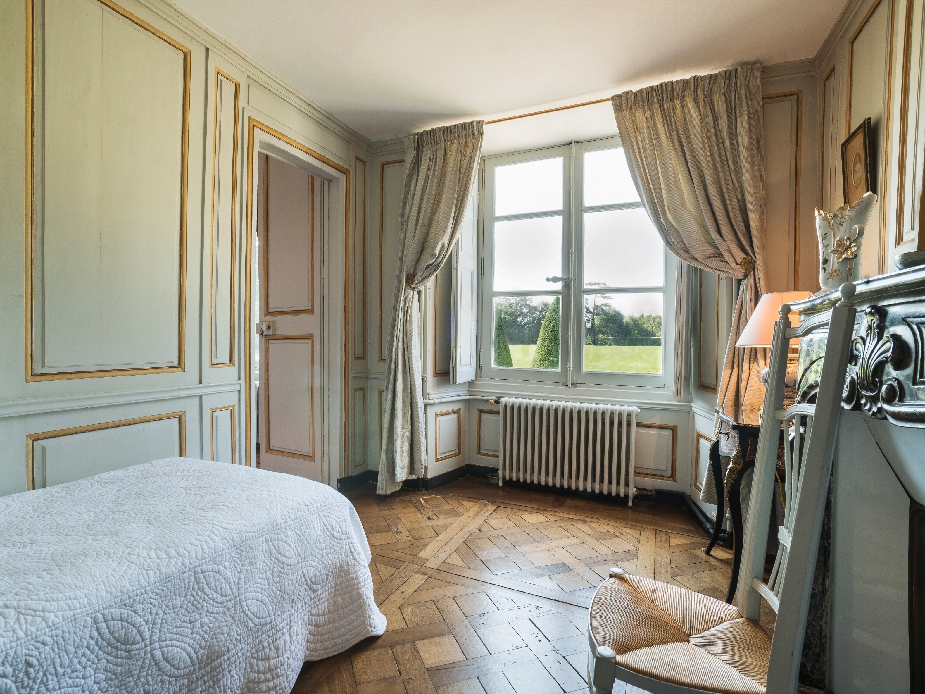 A room with a bed, a chair, a radiator, and a window with curtains.