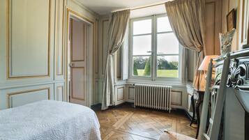 A room with a bed, a chair, a radiator, and a window with curtains.