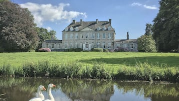 Un grand bâtiment en pierre, doté de nombreuses fenêtres, avec un étang au premier plan.