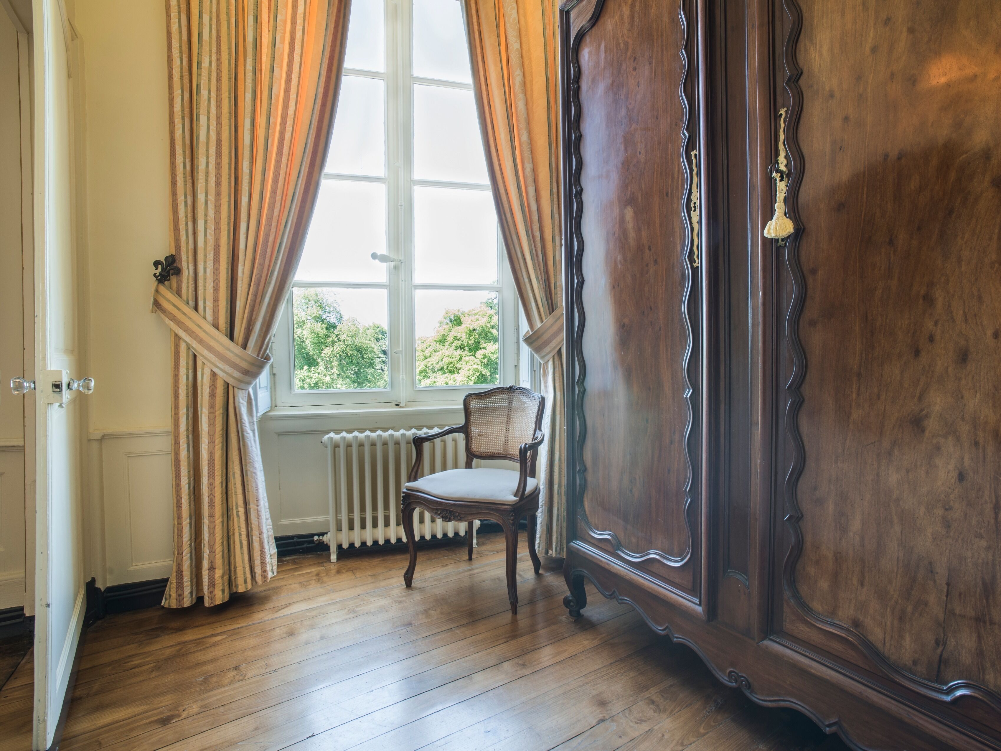 Une pièce avec un plancher en bois, un radiateur, une chaise et une grande armoire en bois.