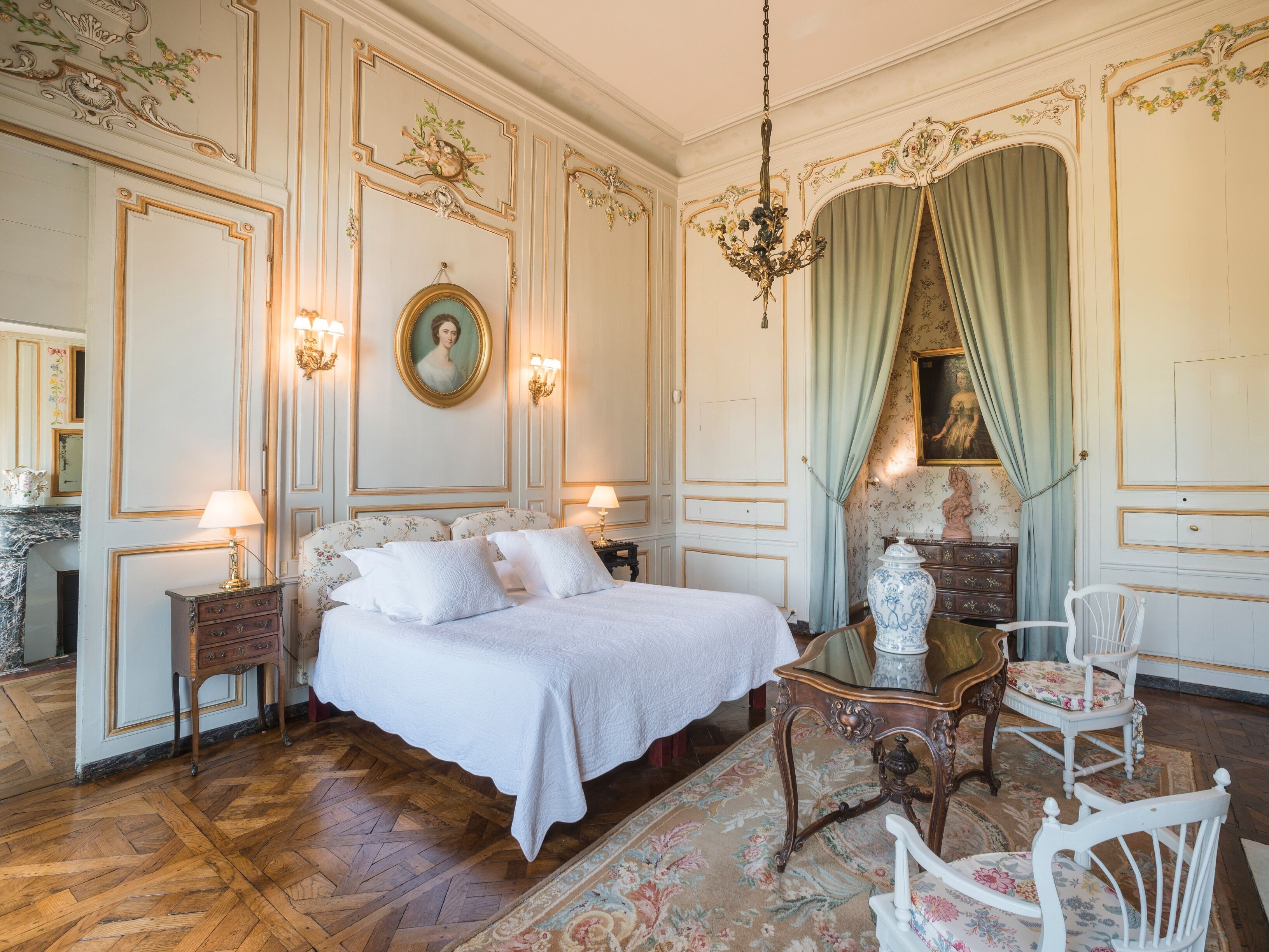 Un dormitorio clásico y elegantemente decorado, con una cama grande, adornos ornamentales en las paredes y un candelabro.