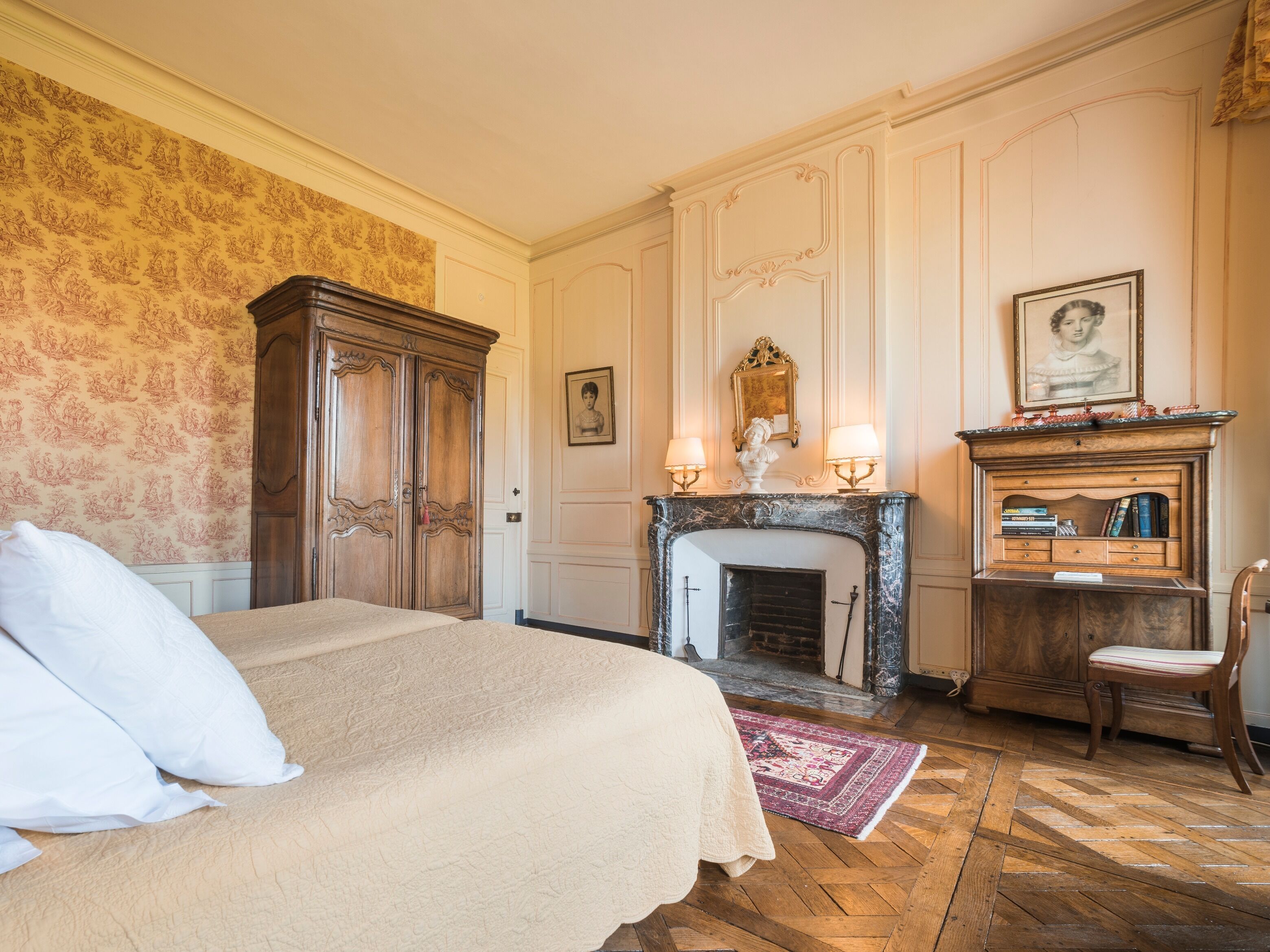 Una habitación clásica con cama, chimenea, aparador de madera y espejo.