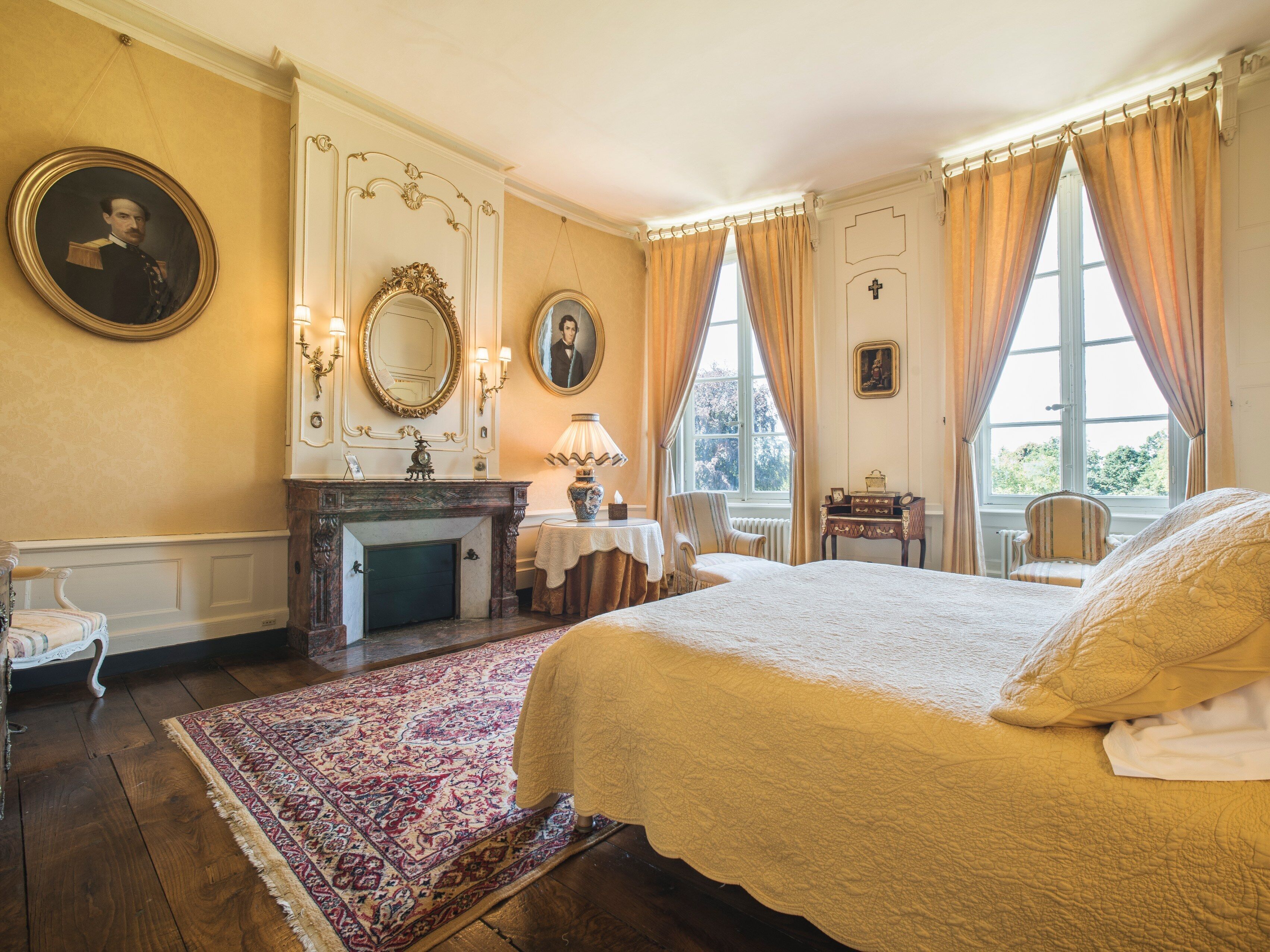 Een klassieke kamer met een groot bed, een open haard, een tafel met een lamp en twee stoelen.
