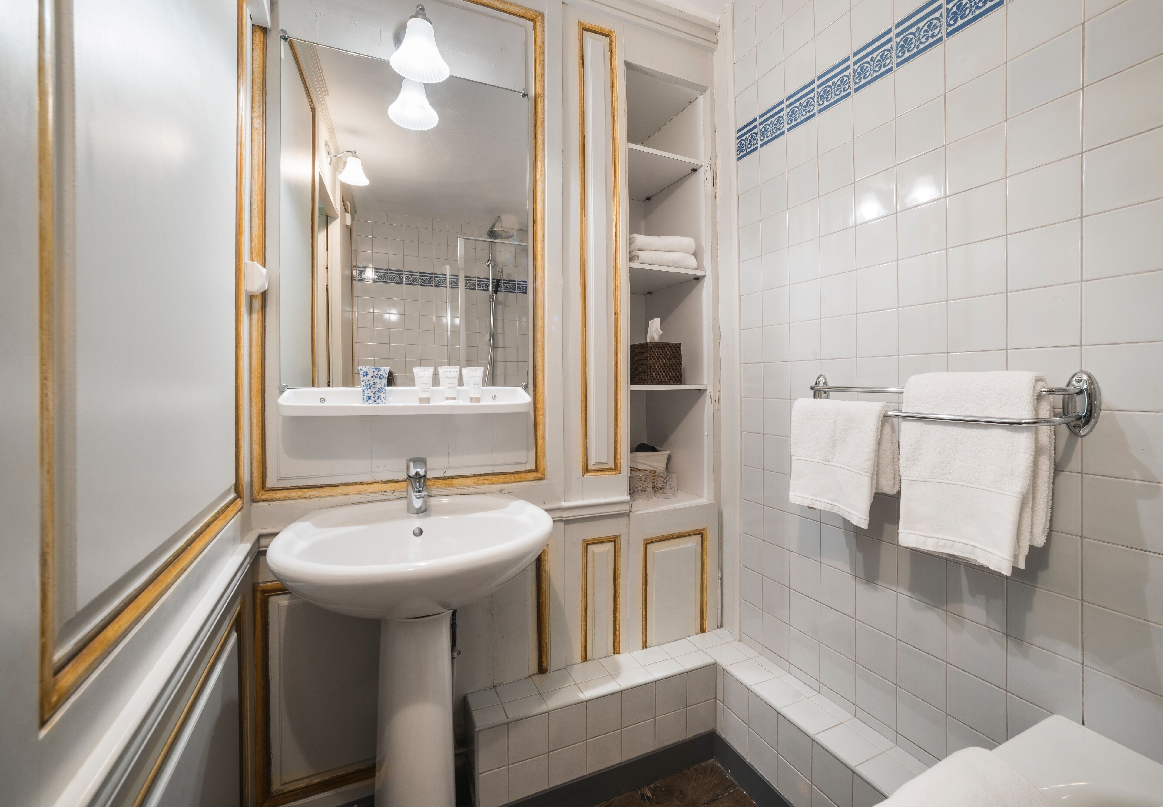 Un baño con lavamanos blanco, espejo y toallero.