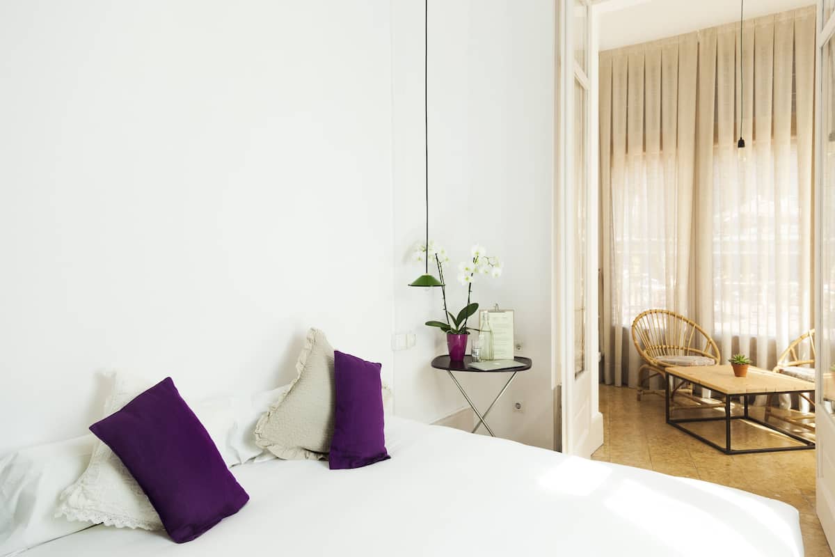 Una camera d'albergo con un letto, due cuscini viola, un tavolino con una pianta e una sedia.