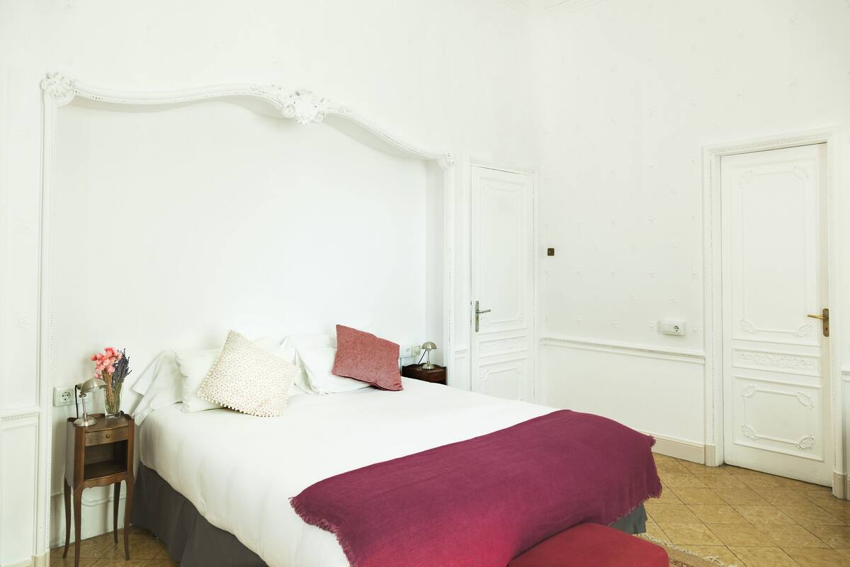 Una camera da letto con un letto bianco, un comodino, una coperta rossa e una porta.