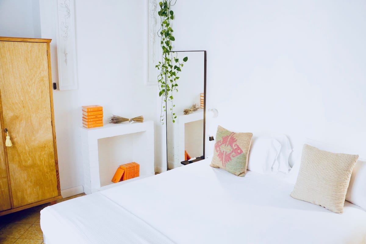 Una camera da letto con un letto, un armadio in legno, uno specchio e un piccolo ripiano con libri e una pianta.