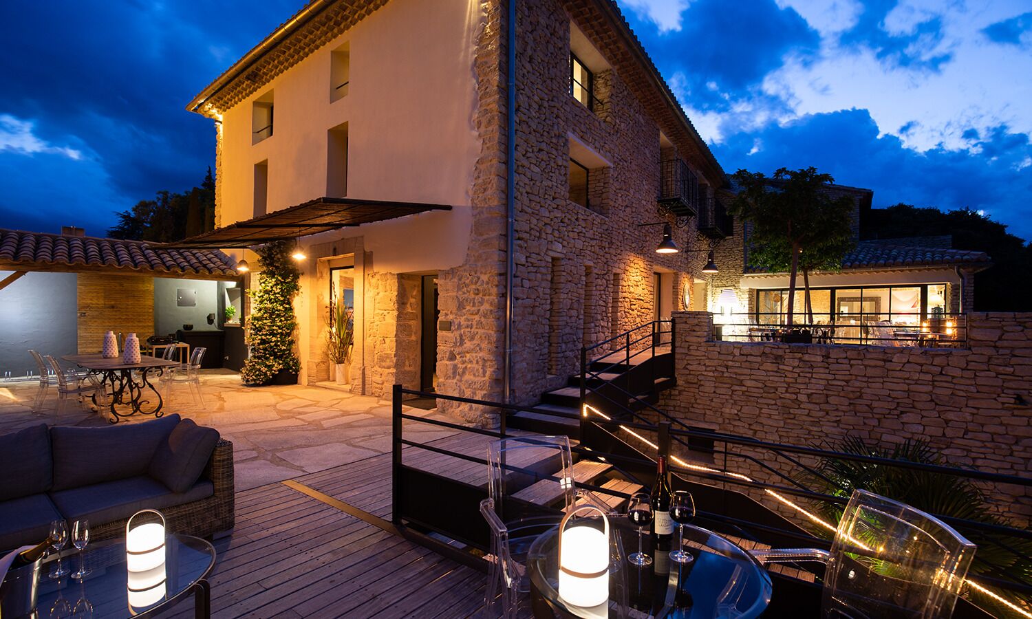A stone building with a patio area, outdoor seating, and a staircase leading to an upper level.