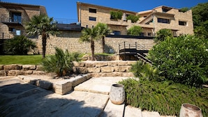 Un bâtiment en pierre doté de nombreux balcons et d’un jardin bien entretenu, agrémenté de palmiers et d’arbustes.