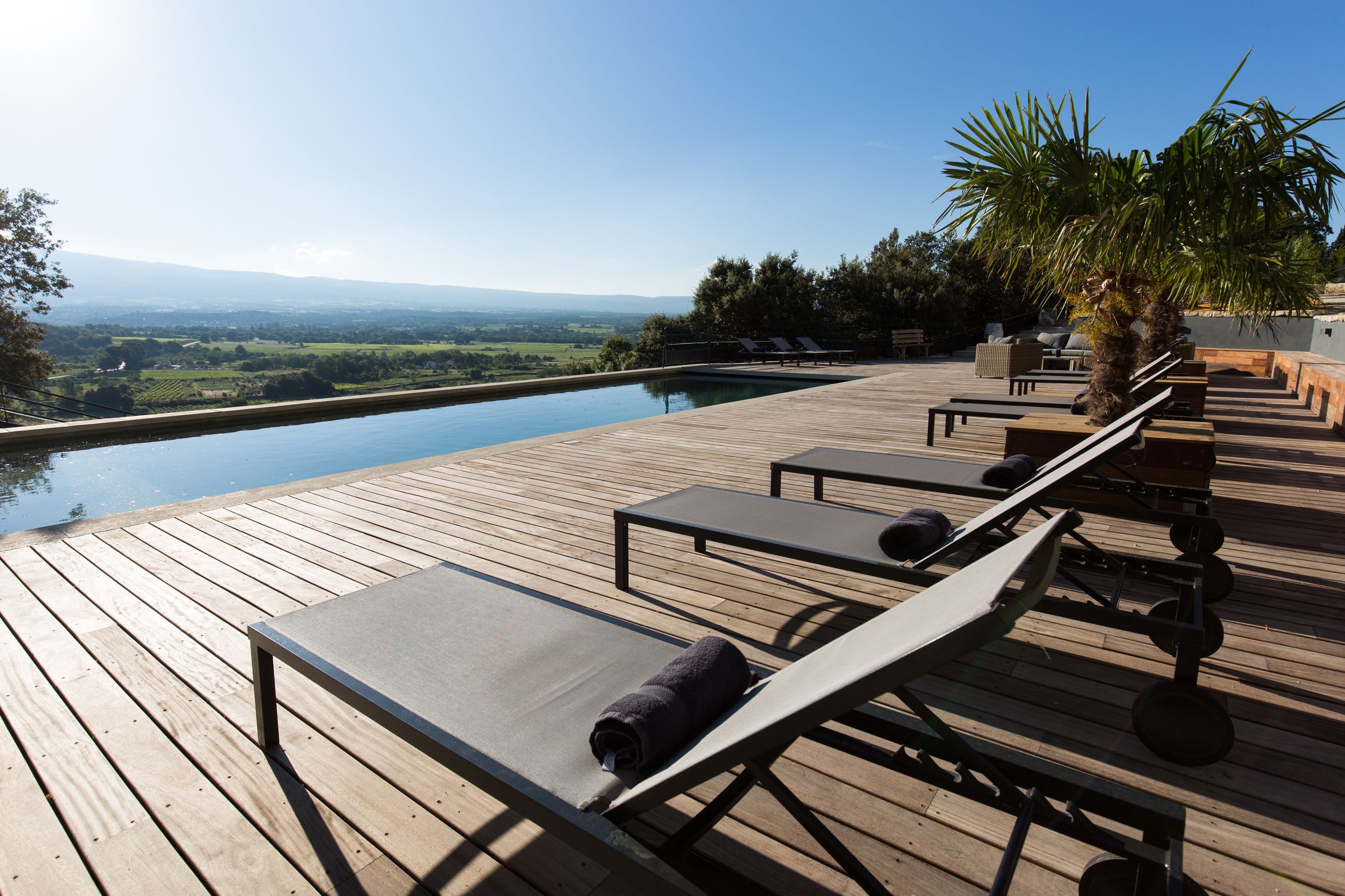 Una terraza de madera con tumbonas y una piscina con vistas a un paisaje pintoresco.